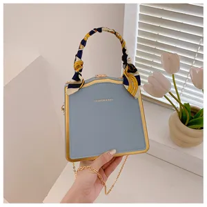 Sac de soirée structuré bleu clair chic avec cadre doré, poignée foulard et bandoulière chaîne.