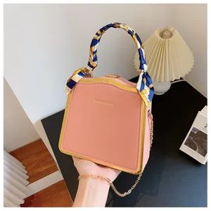Détail de sac à main rose avec cadre doré, poignée en foulard de soie et bandoulière chaîne.