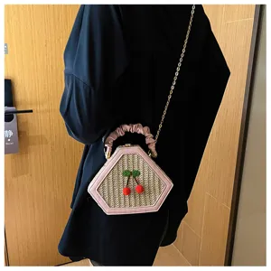 Chic hexagonal straw crossbody bag with pink leather trim, cute cherry decor, and chain.