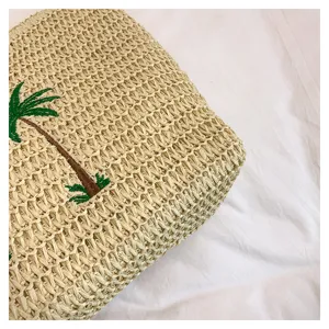 Closeup detail of handmade straw woven beach vacation tote bag with palm tree embroidery.