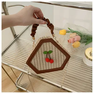 Detail view of woven straw crossbody bag with chic pleated handle and cute cherry accent.
