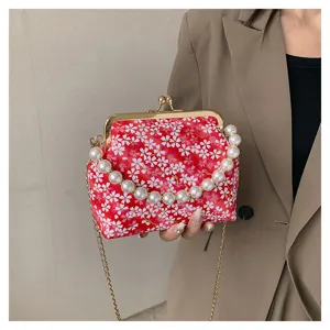 Close-up of red floral kiss-lock handbag with faux pearl handle and gold chain strap.