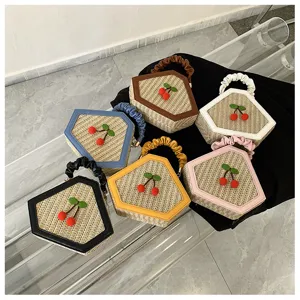 Close-up detail view of stylish woven straw handbags featuring cute cherry decor and ruffled handles.