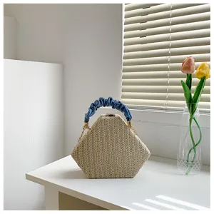 Detailed shot of a stylish hexagonal straw woven handbag with blue ruched leather handle.