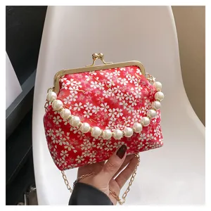 Detail view of the red floral kiss-lock bag featuring a elegant pearl handle and gold chain strap.