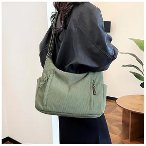 Green corduroy shoulder bag detail shot showing textured fabric, spacious interior, and zipper.