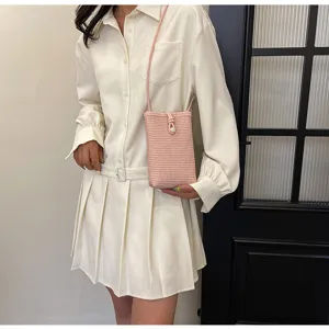 Detailed view of the pink woven straw phone bag, casual crossbody design with pearl accent.