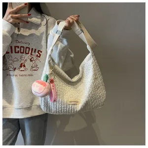 Close-up of white crinkled hobo shoulder bag with cute plush peach charm and woven label.