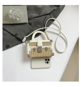 Sac bandoulière élégant en paille tissée avec bordure en cuir et coins métalliques pour femmes.
