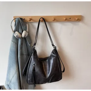 Vue détaillée du sac porté épaule hobo en cuir noir vintage sur une étagère en bois.