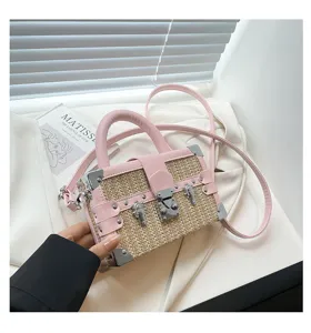 Vue détaillée du sac à main boîte malle en paille rose avec coins métalliques et fermoir sécurisé.