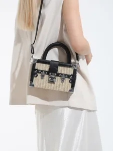 Sac bandoulière boite en paille tressée chic avec bordure en cuir et coins métalliques.