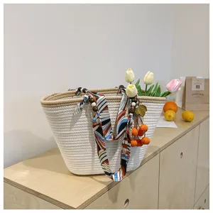 Woven tote bag detail showing colorful scarf ribbon and cute orange charms on wooden shelf.