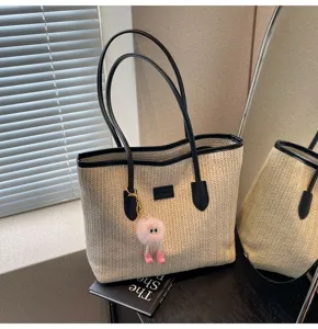 Detailed view of the woven straw tote bag with black leather handles and pink plush charm.