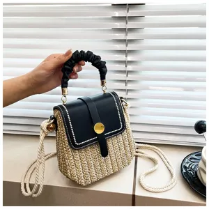 Detail view of woven straw crossbody bag with black top handle and metal clasp.