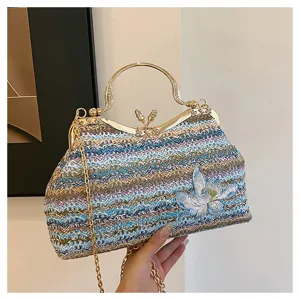 Detailed view of colorful woven handbag, gold metal kiss lock, blue flower embroidery, chain.