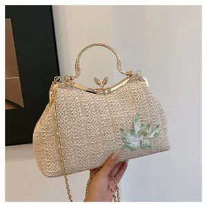 Close-up detail of straw woven handbag with metallic gold clasp and floral embroidery.