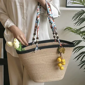Woven straw tote bag with scarf ribbon handle and floral pendant for summer beach vacation.