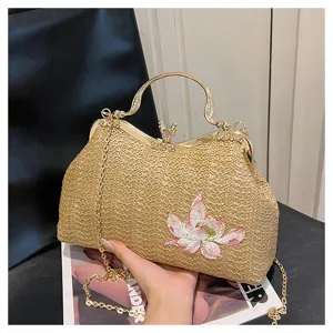 Detail view of woven straw crossbody bag with gold handle and lotus embroidery design.