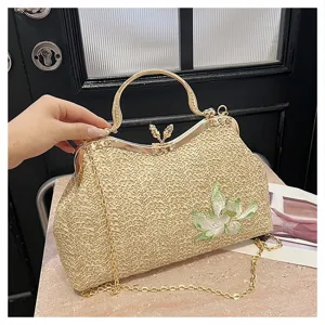 Woven straw handbag detail showing gold metal frame handle, chain strap, and embroidered flower.