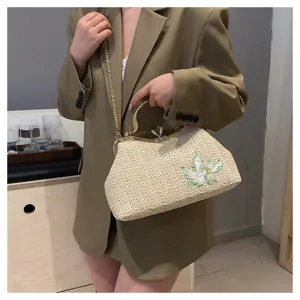 Detail view of a stylish straw woven handbag with metal frame, chain strap and floral embroidery.