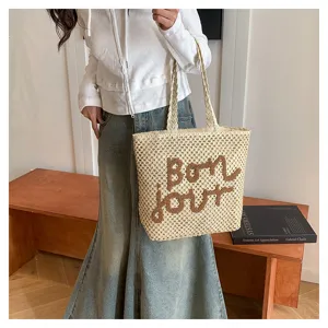 Woven straw tote bag with brown embroidered letter detail, stylish shoulder beach bag for women.