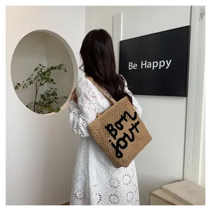 Detail of straw woven tote bag with black letter embroidery for stylish summer beach vacation use.