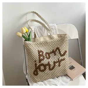 Trendy hollow straw woven shoulder bag with brown embroidery letters for women beach vacation.