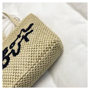 Detail view of woven straw beach tote bag with dark embroidery texture and hollow design.