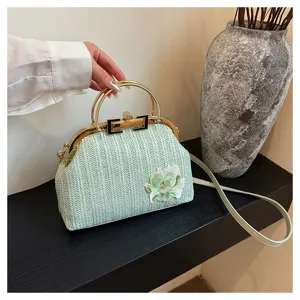 Gros plan sur le sac à main tissé vert clair avec broderie florale et cadre en métal.