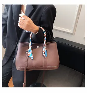 Detail de sac cabas en cuir marron avec poignee foulard en soie et sangle pour bureau chic.