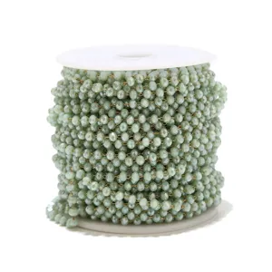 Light green crystal bead chain detail, sparkling faceted beads on spool for DIY jewelry making.