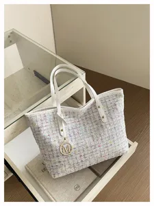 Detail view of stylish tweed tote bag with chic white leather handles and metallic charm.