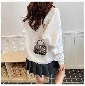 Mini metallic pleated crossbody bag with top handle and chain strap worn by model in room.