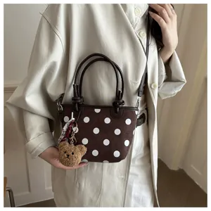 Vista dettagliata della borsa a secchiello a pois marrone con ciondolo orsetto di peluche e manici.