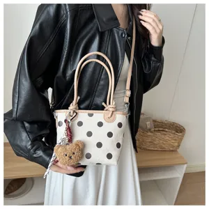 Dettaglio ravvicinato della elegante borsa a secchiello in tela a pois con portachiavi orsetto.