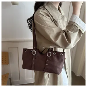 Nahaufnahme der braunen Wildleder-Schultertasche mit Metallösen und doppelten Schnallen.