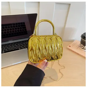 Detail shot of a metallic gold mini pleated handbag with round metal handle and chain strap.