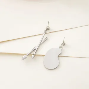 Unique asymmetric paintbrush and palette stud earrings, silver-tone artistic jewelry.