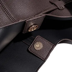 Bruine tas van zacht leer met magnetische drukknoop detail, premium textuur en stiksels.