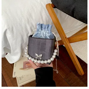 Detail view of the trendy bucket bag featuring denim drawstring, pearl handle and butterfly.