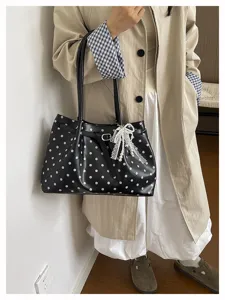 Dettaglio della borsa a spalla nera a pois con fiocco di perle e fibbia elegante.