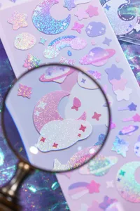 Holographic journaling sticker detail shot, cute cosmic elements, shiny PVC flash film finish.
