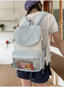 Detail shot of the light blue and white canvas backpack with transparent front pocket and charm.