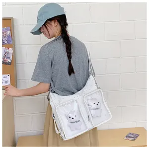 Detailed view of white ita bag with transparent pockets and cute bear dolls, worn by model.