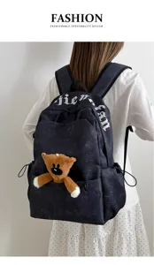 Vista detallada de mochila de lona estilo coreano con colgante de osito y letras góticas.