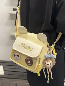 Détail de sac bandoulière jaune en toile, ita bag avec oreilles d'ours, poche transparente et pins.