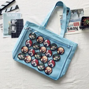 Detail view of light blue canvas ita bag featuring clear window and anime character pins inside.