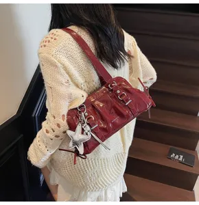 Red patent leather shoulder bag detail showcasing metal buckle and stylish star pendant accessory.