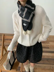 Detailed shot of the stylish knit striped scarf featuring soft texture and cute pom-poms.